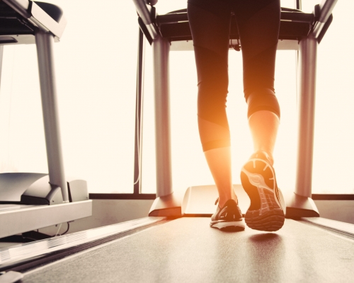 Lower body at legs part of Fitness girl running on running machine or treadmill in fitness gym with sun ray. Warm tone. Healthy and Exercise activity concept. Workout and  Strength training theme.