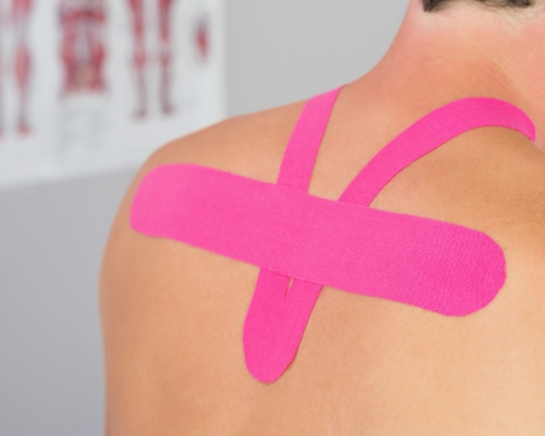 Close up of male patients back with applied pink kinesio tape in bright office